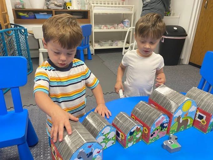 Two children play with colorful toy houses in a classroom, arranging them in a row.