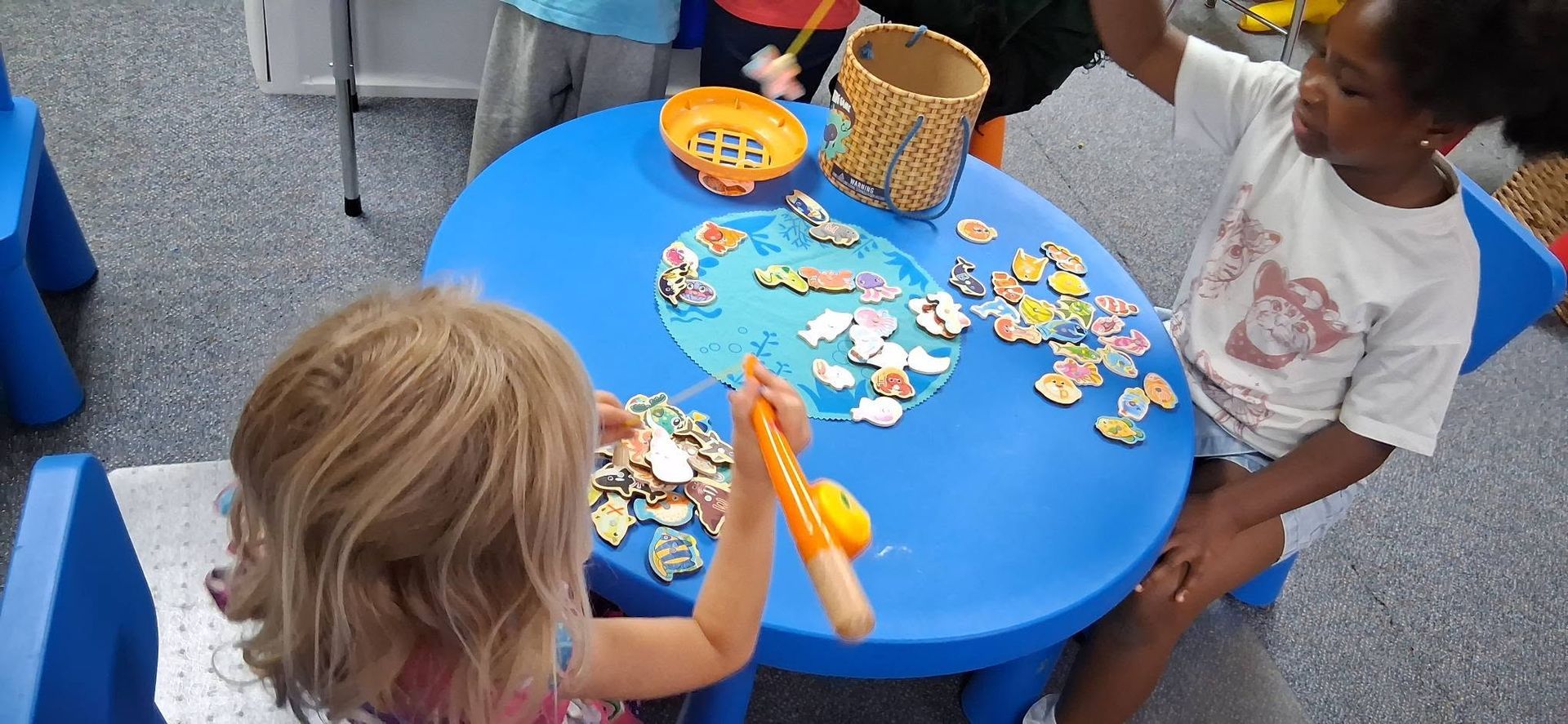 Children playing with seashells and toy fish around a blue table at a seaside activity area