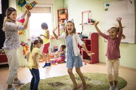 Children playing and dancing in a colorful playroom with toys scattered around