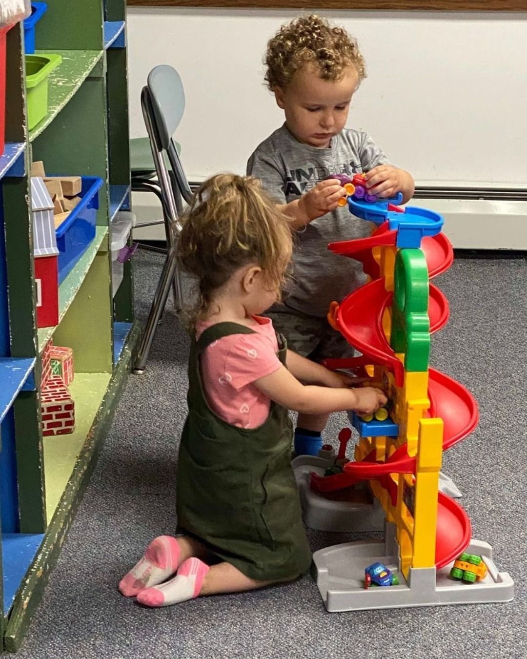 Two toddlers playing with a colorful marble run on a classroom floor