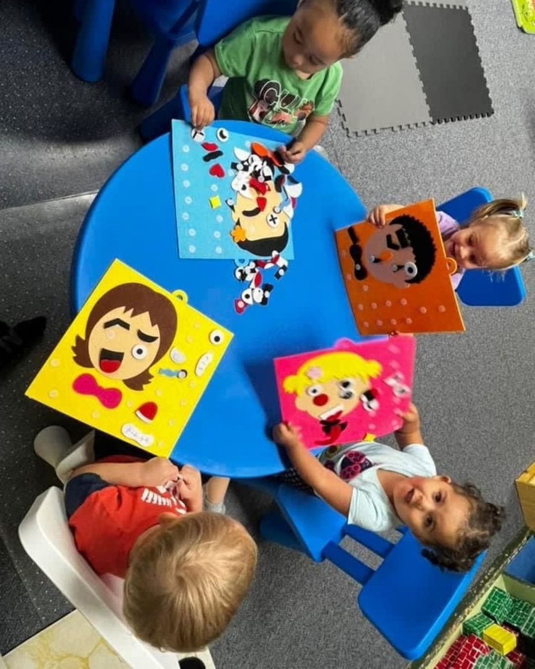 Children seated around a blue table, assembling colorful puzzles in a classroom.