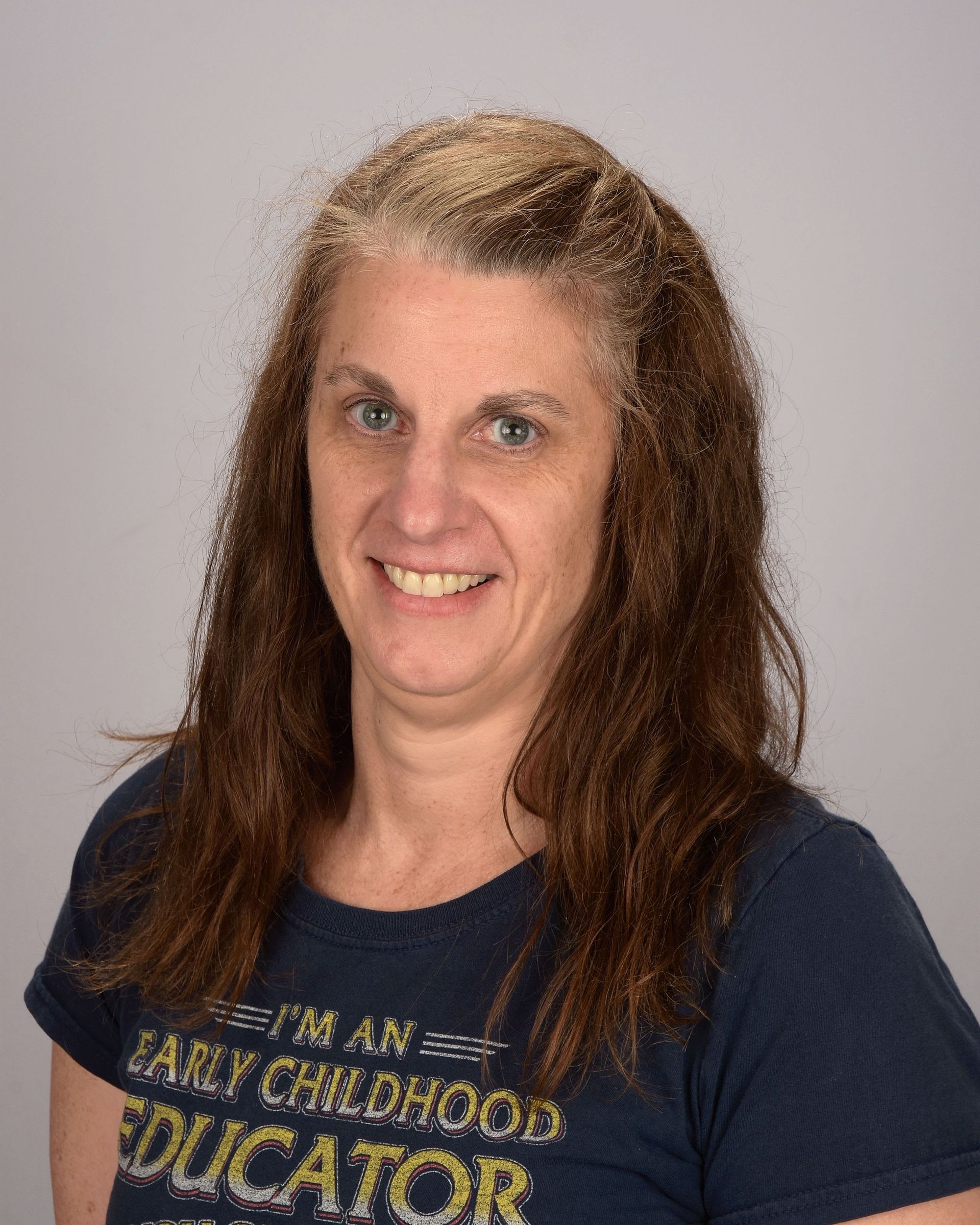 Smiling woman with long brown hair wearing a navy T-shirt against a plain light background