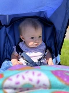 Baby sitting in a blue stroller, looking to the side, with a colorful blanket in the foreground