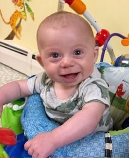 Smiling baby sitting in a colorful activity seat with patterned blue padding