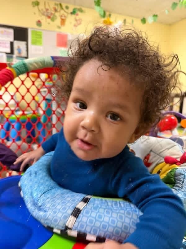 Smiling child in a blue sweater lying on a colorful cushion in a play area
