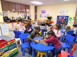 Children seated at blue tables doing a classroom activity in a colorful preschool room