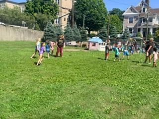 Children playing on a grassy field near houses on a sunny day