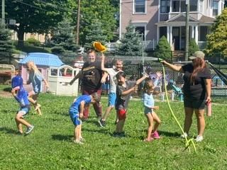 People playing with water balloons on a grassy lawn outside apartment buildings
