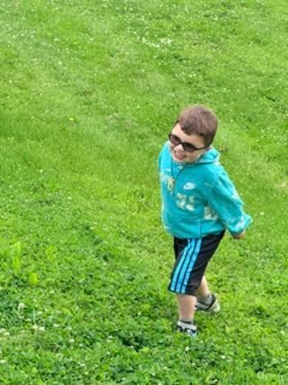 Boy in sunglasses and a blue jacket walking on a grassy hill.