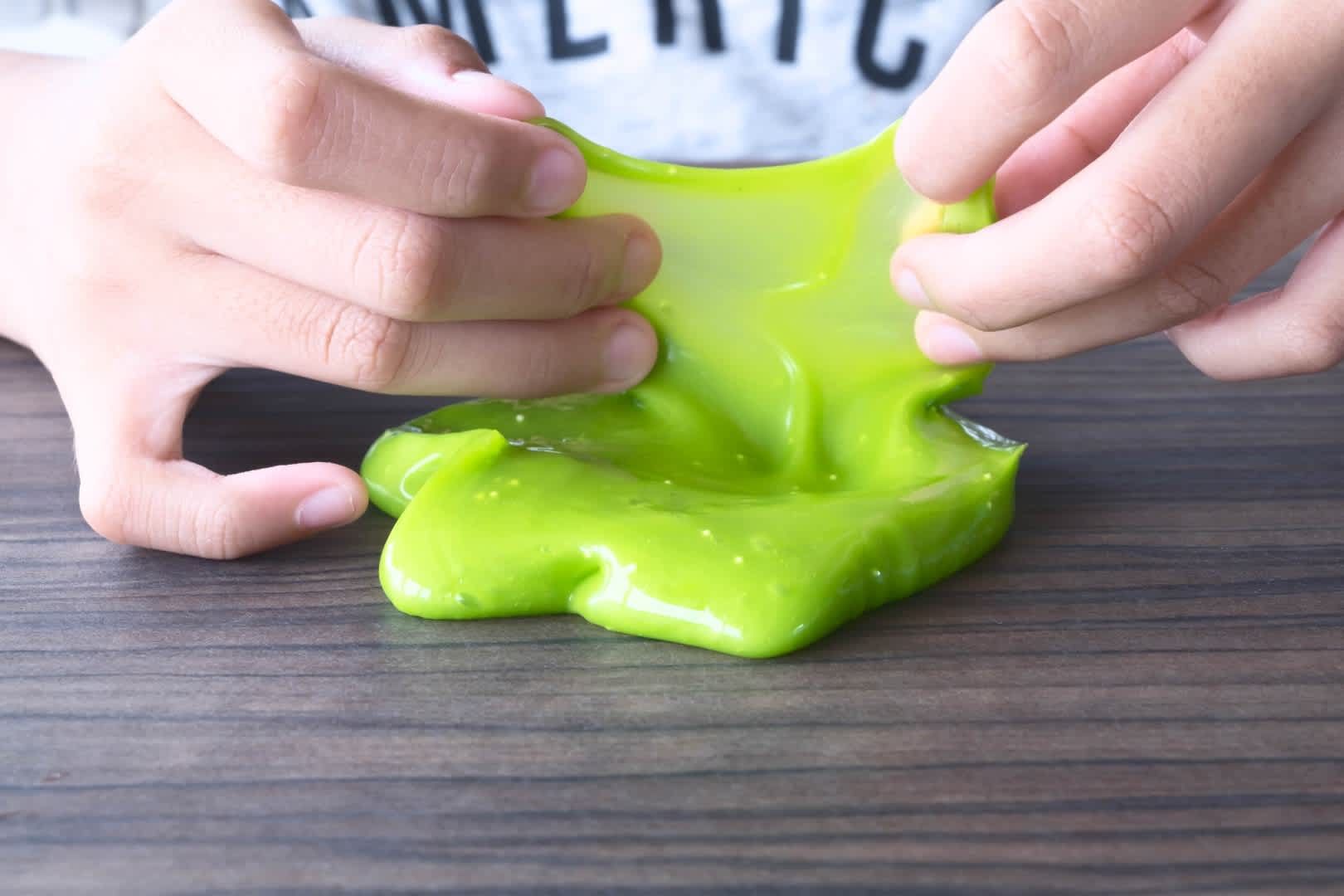 Hands stretching bright green slime on a wooden table