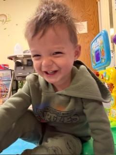 Smiling toddler in a green hoodie playing indoors with colorful toys nearby
