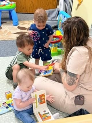 Adult sitting with three young children playing with toys on the floor in a colorful room