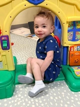 Child sitting and smiling in a colorful plastic play tunnel on a patterned rug