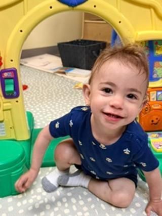Toddler in a blue shirt crawling and smiling under a yellow play tunnel.