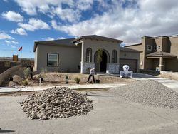 New house under construction with gravel piles and workers in a sunny residential neighborhood