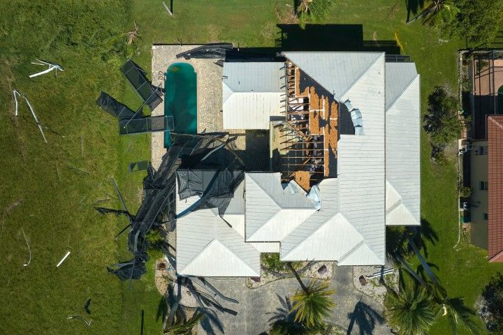An aerial view shows a damaged home with a collapsed pool screen enclosure and a section of missing roof.