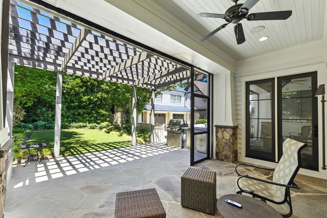 A patio featuring a stone floor, a wooden pergola, a ceiling fan, and patio furniture overlooking a green backyard.