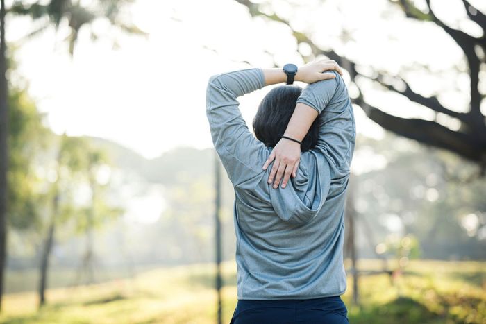 a woman wearing a watch stretches her arms in a park