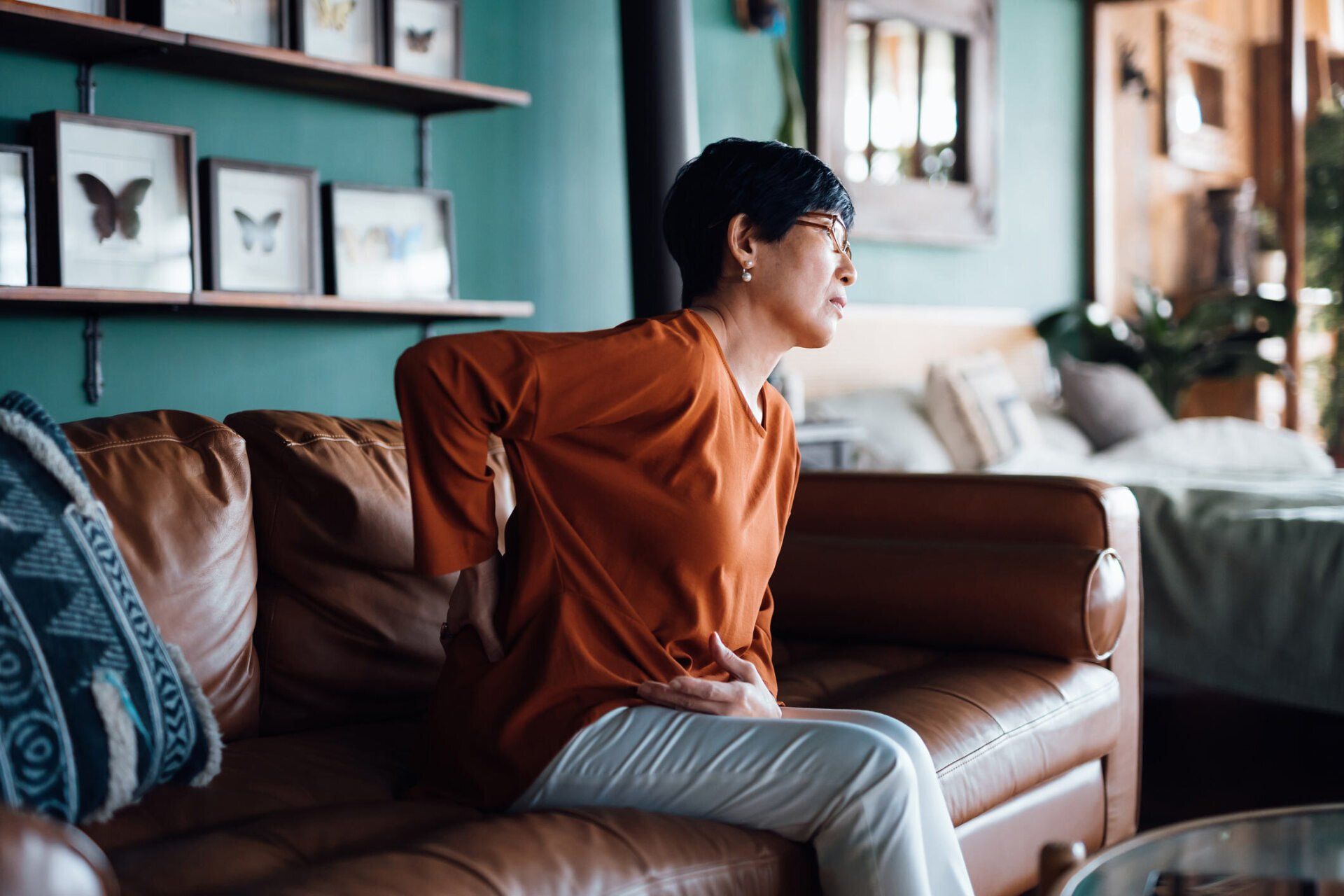 a woman sits on a couch holding her back in pain