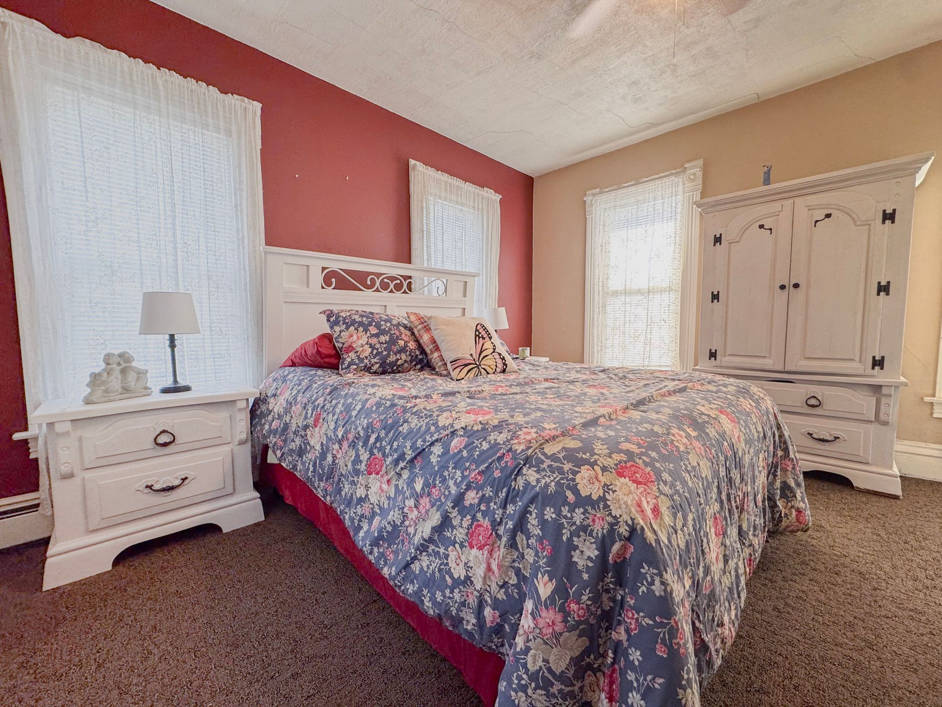 Cozy bedroom with pink walls, floral bedspread, white nightstands, and a large armoire