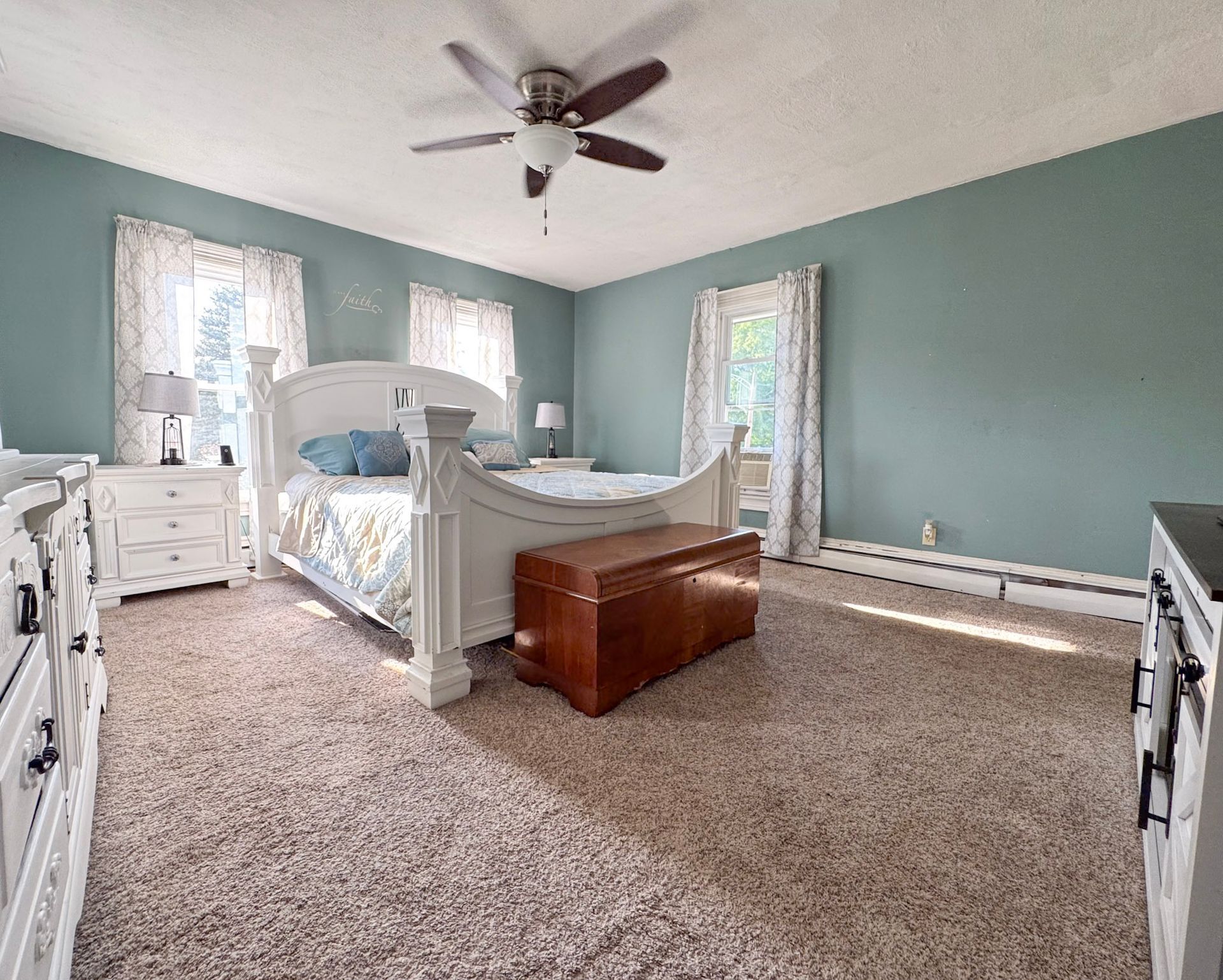 Spacious bedroom with white furniture, teal walls, carpet, and a wooden chest at the foot of the bed.