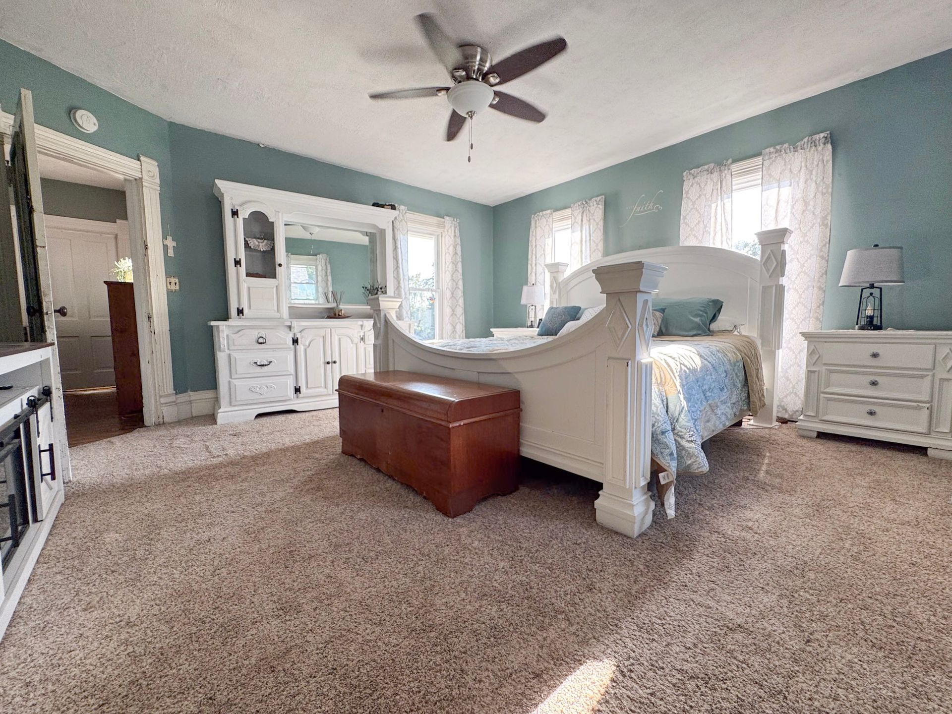Bright bedroom with white furniture, light blue walls, and a carpeted floor, viewed from the doorway.