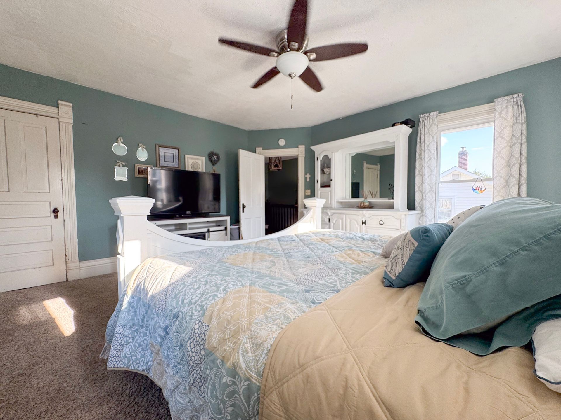 Bedroom with teal walls, white furniture, ceiling fan, and a bed with blue and tan bedding.