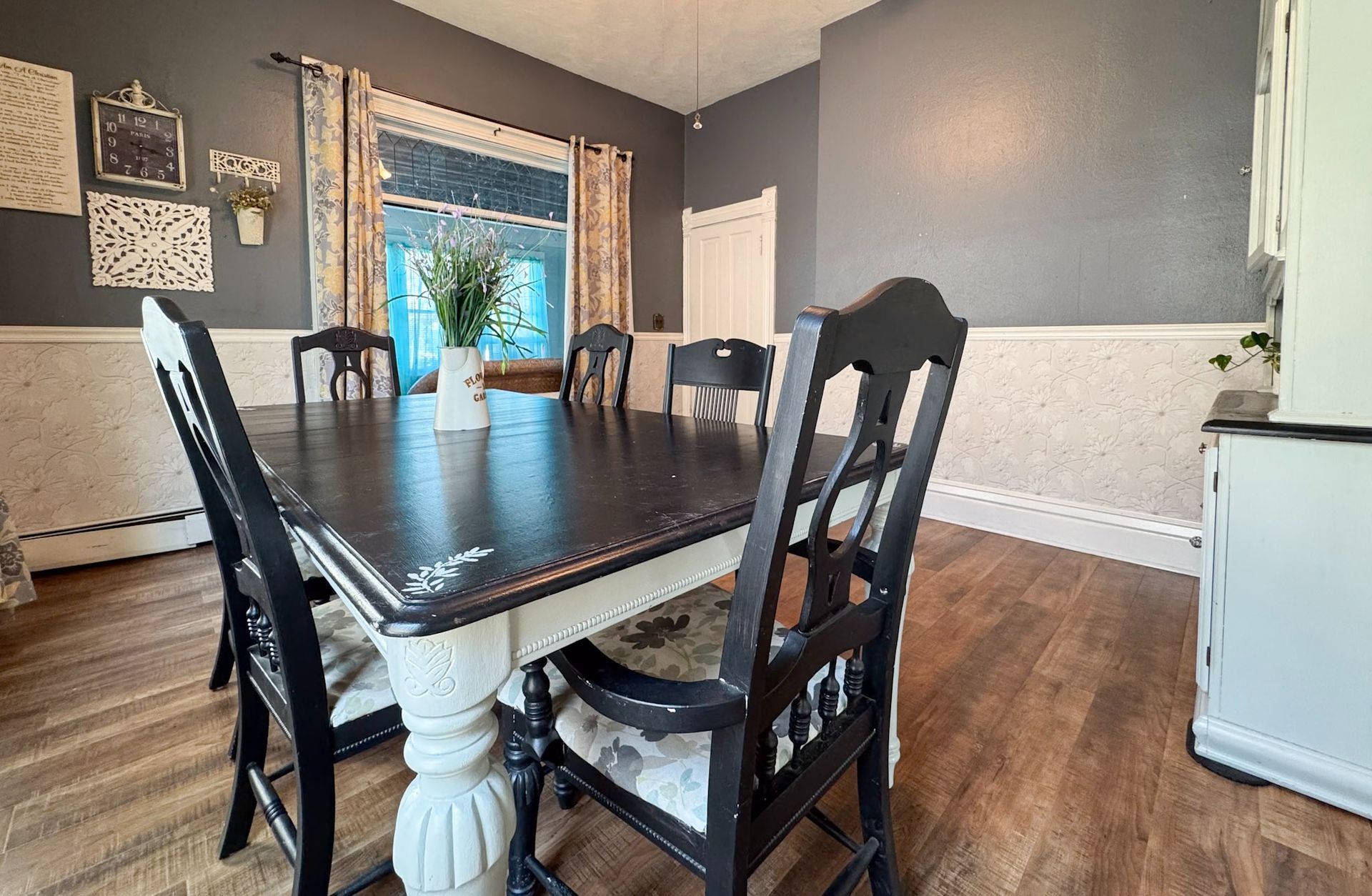 Dining room with dark table, mixed chairs, gray walls, and a window with a plant.