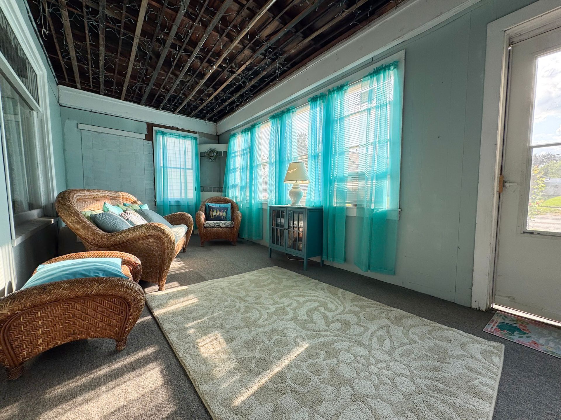 Bright sunlit room with wicker chairs, turquoise curtains, and a patterned rug.