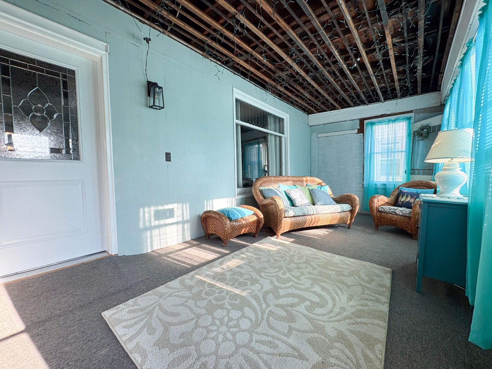 Sunroom with wicker chairs, blue walls, white rug, and exposed ceiling beams.