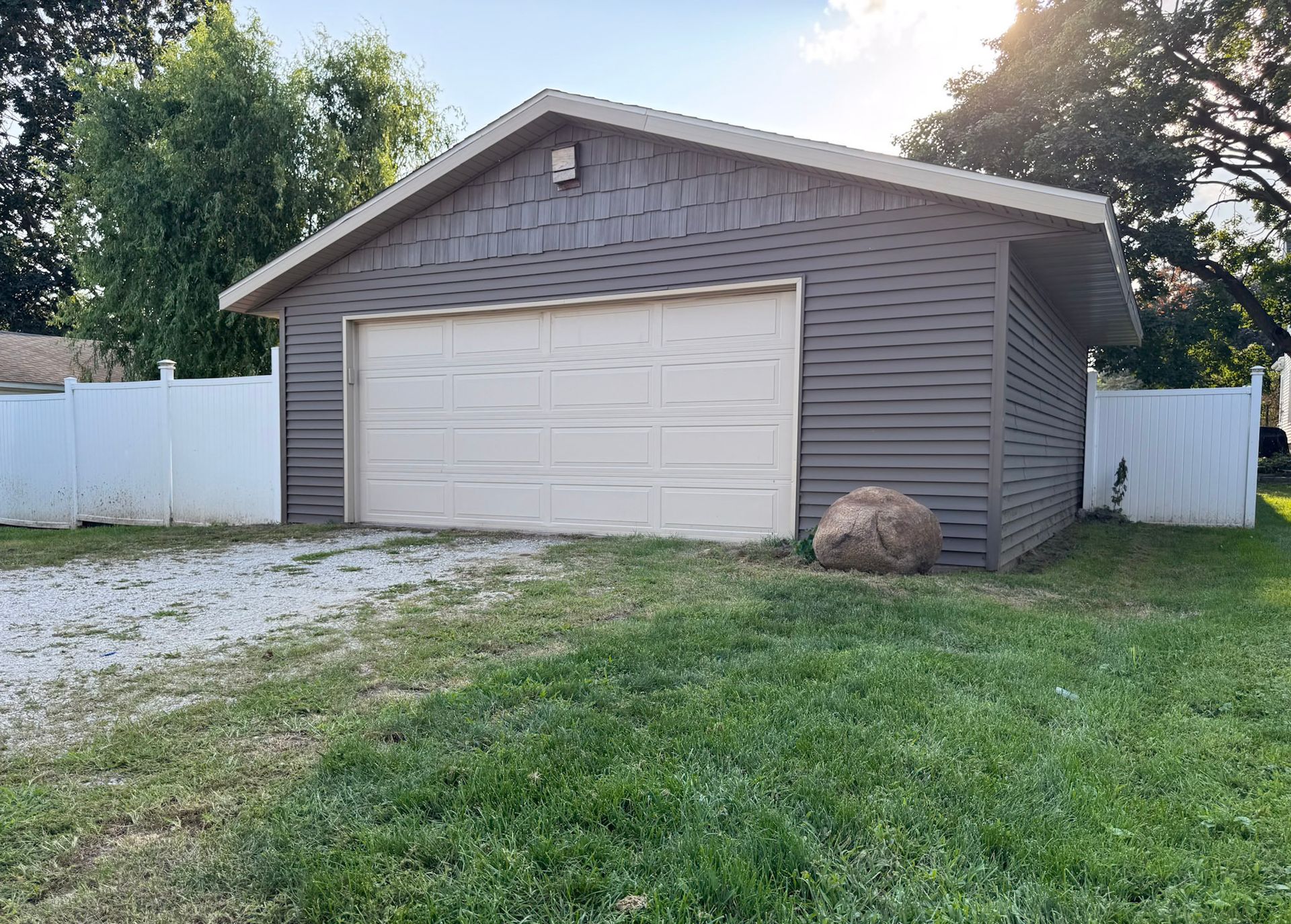 Detached gray garage with white door beside a grassy yard and white fence