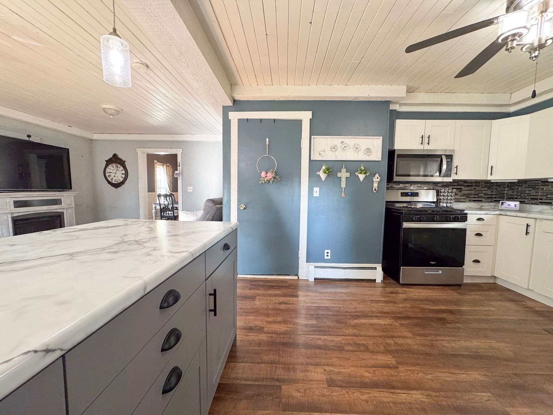 Bright kitchen with blue island, white cabinets, black appliances, and wood floors.