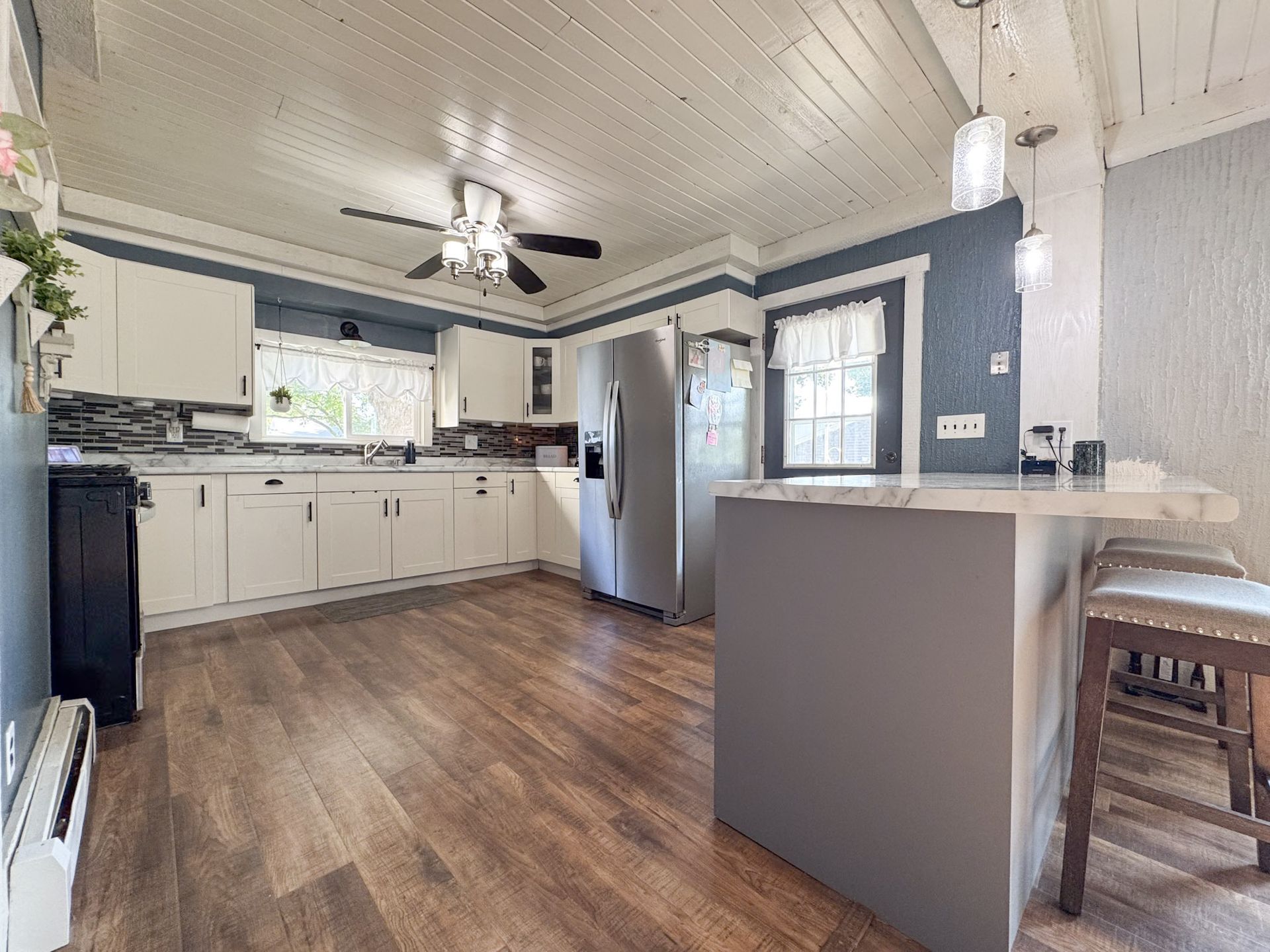Bright kitchen with white cabinets, wood-look floor, island, stainless fridge, and blue accent wall