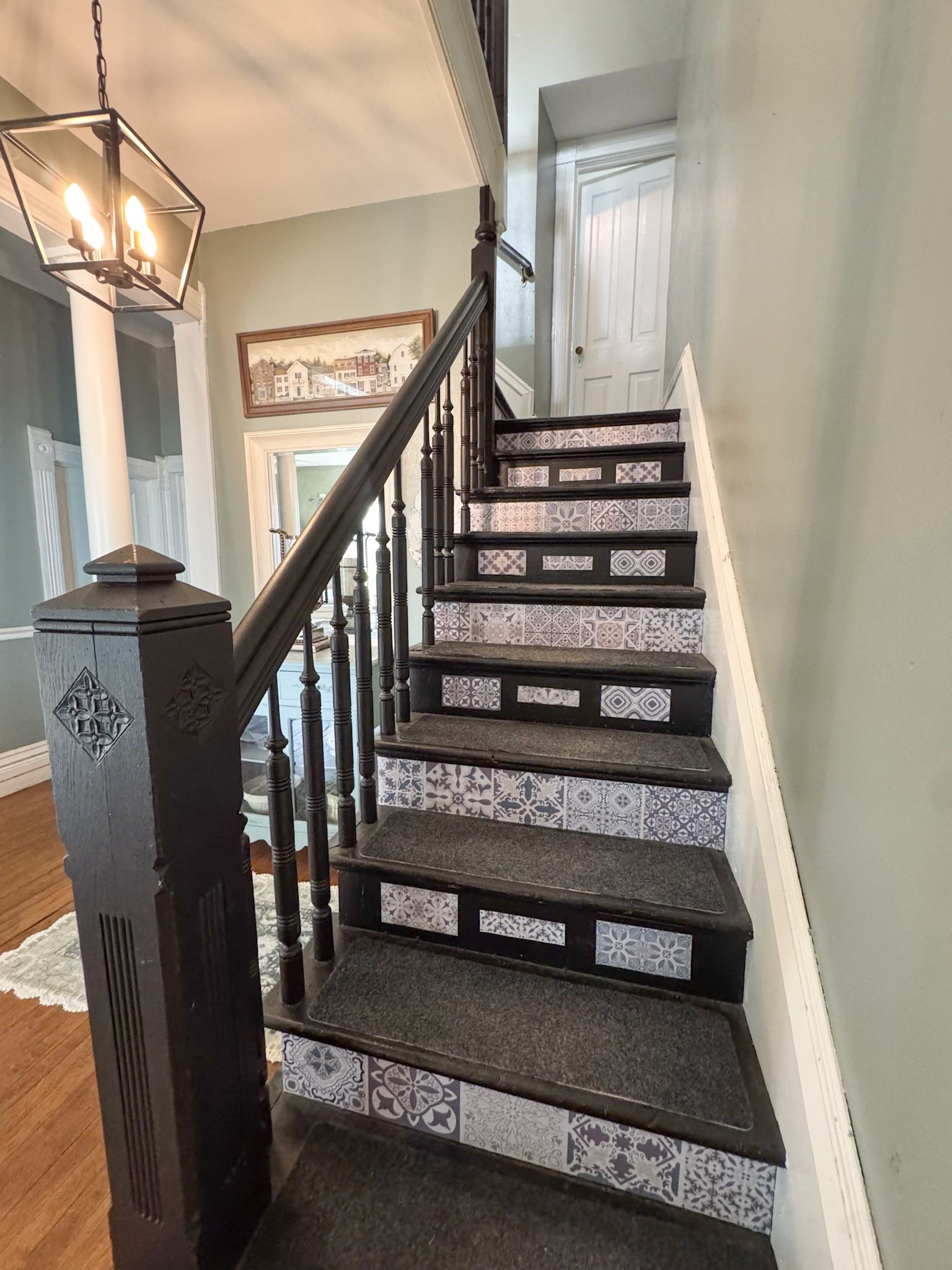 Narrow carpeted staircase with dark railings leading to a white door in a hallway