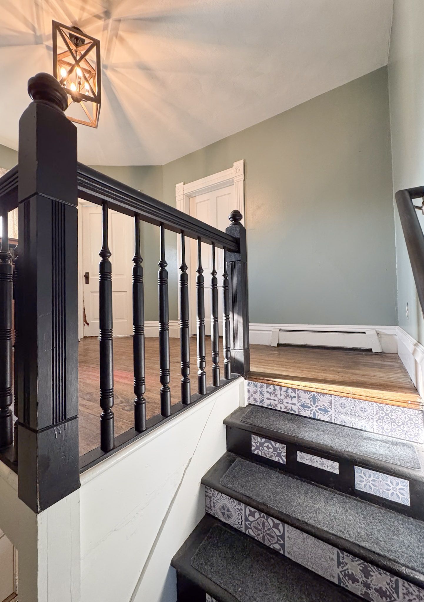Carpeted staircase with dark railing leading to a green-walled upstairs landing and wall sconce light