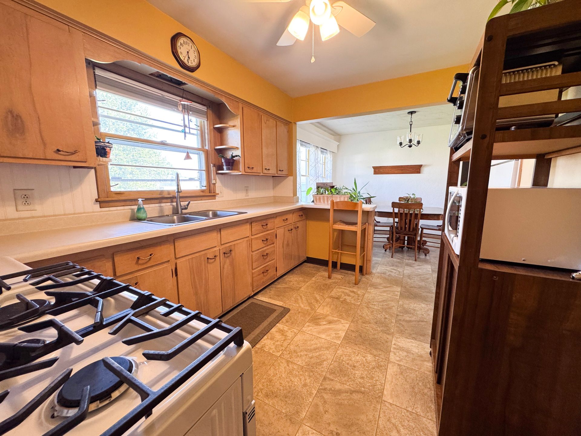 Warm kitchen with wooden cabinets, gas stove, sink, and a dining area beyond the counter.