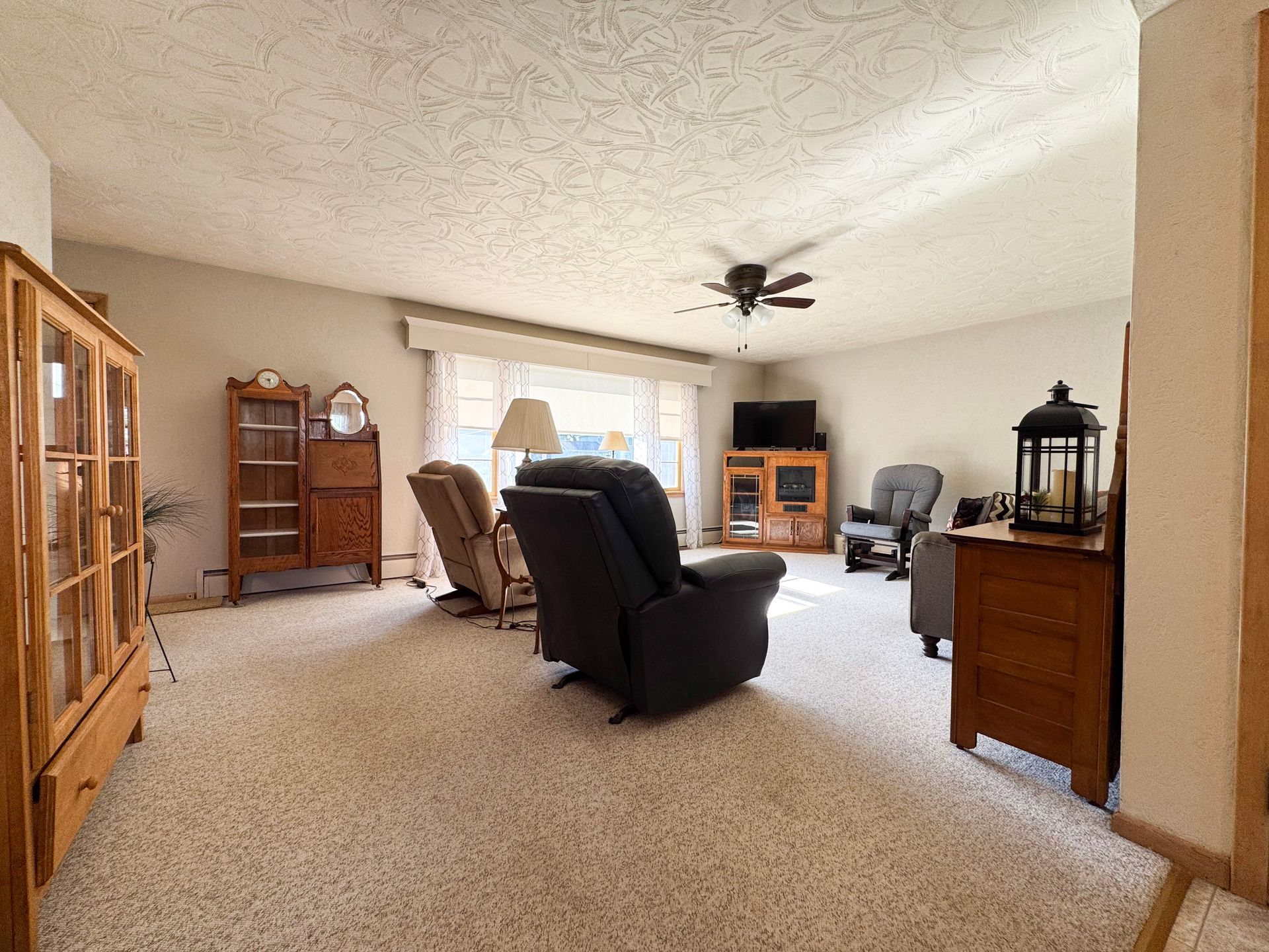 Spacious beige living room with recliners, wood furniture, ceiling fan, and a fireplace