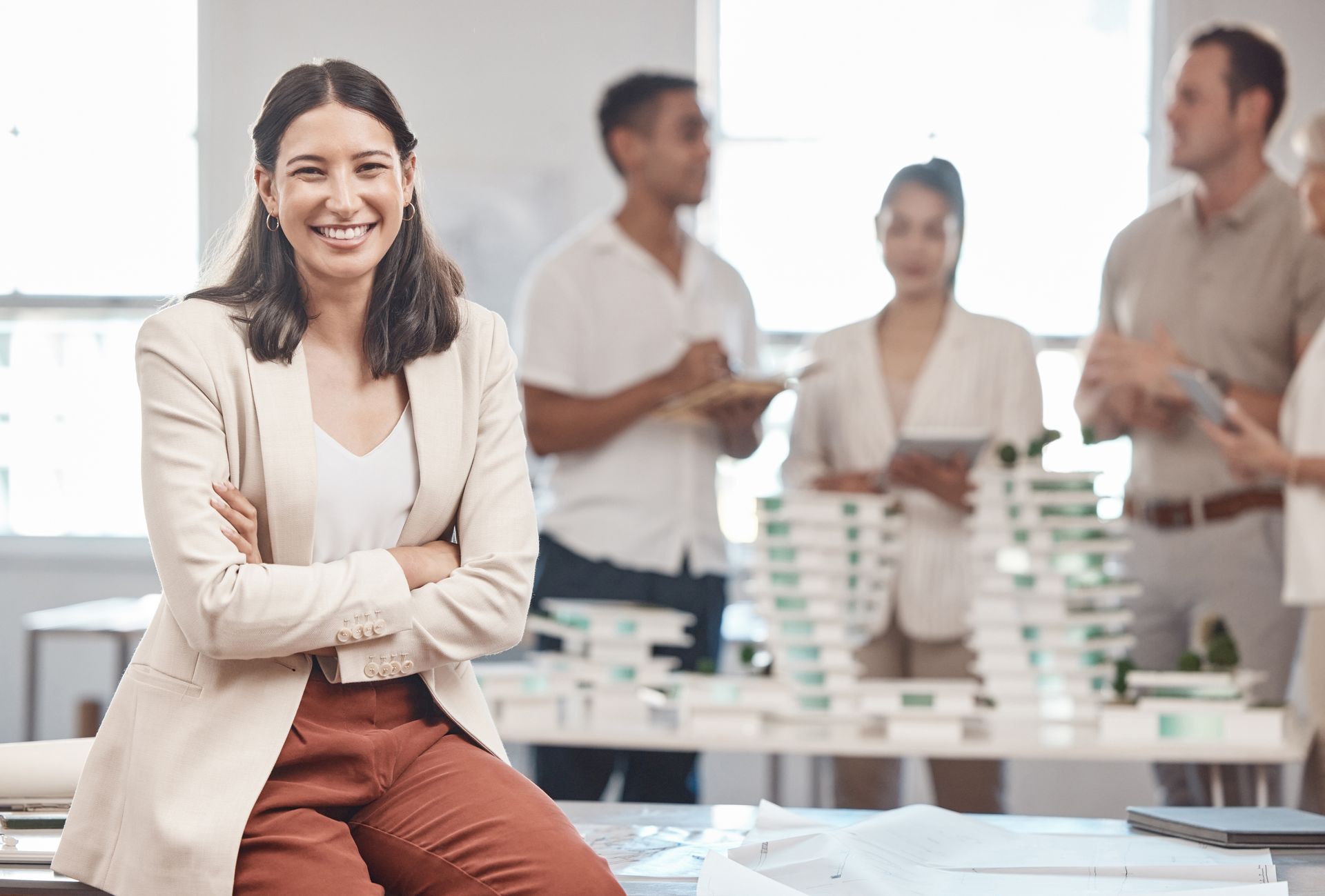 A woman is sitting on a table with her arms crossed in front of a group of people as a strong leader