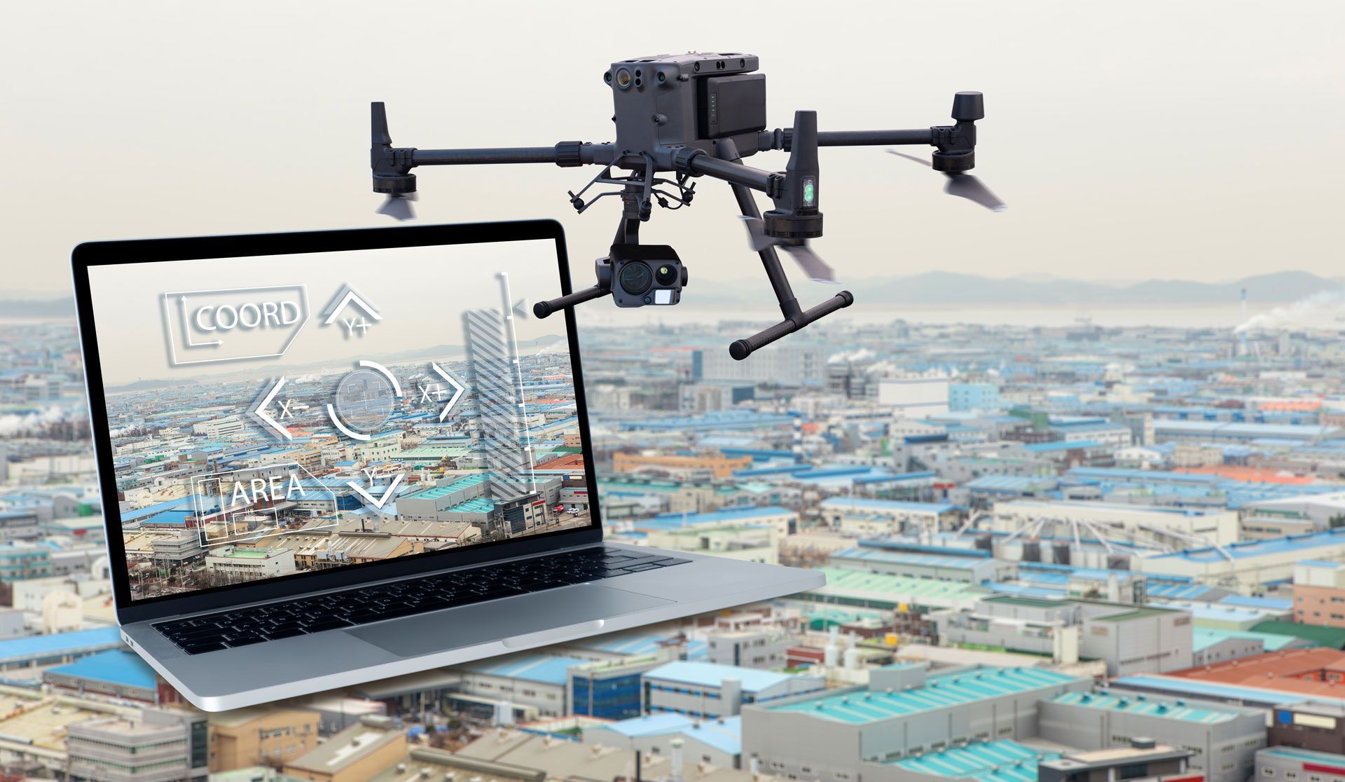 Drone flying above a laptop displaying a city map over a sprawling urban landscape