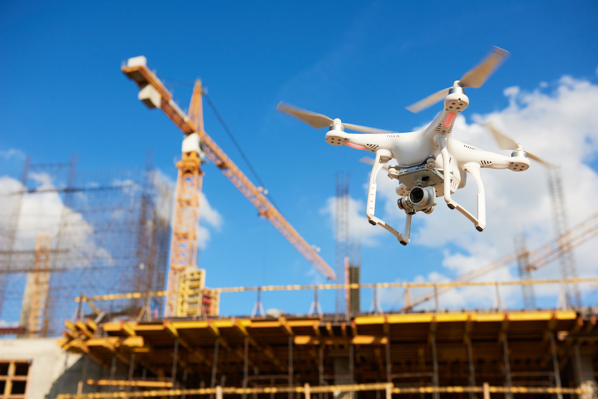 White drone flying above a construction site with cranes and scaffolding under a blue sky