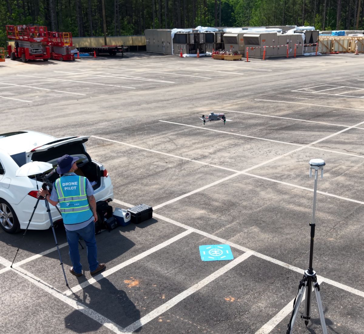 Drone operator beside a white car in a parking lot, monitoring a drone in flight