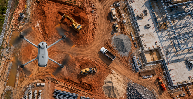 Aerial view of a construction site with excavators, dirt roads, and a partially built concrete structure.