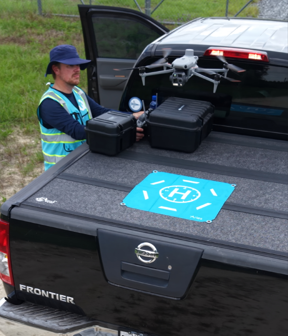 Man loading a drone and cases into the open bed of a black Nissan Frontier truck