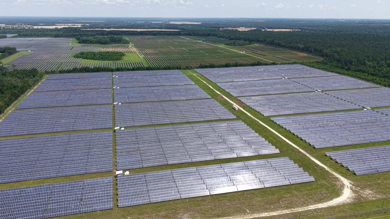 Aerial view of a large solar farm with rows of blue-gray solar panels in open fields.