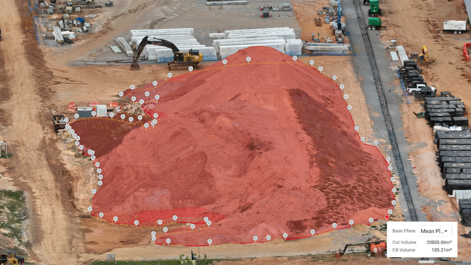 Aerial view of a large red dirt mound at an industrial construction site with equipment and vehicles nearby