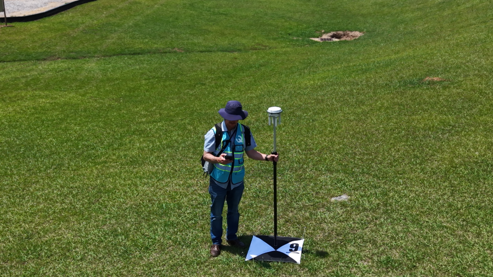 Survey worker standing on grass beside a tripod instrument in an open field