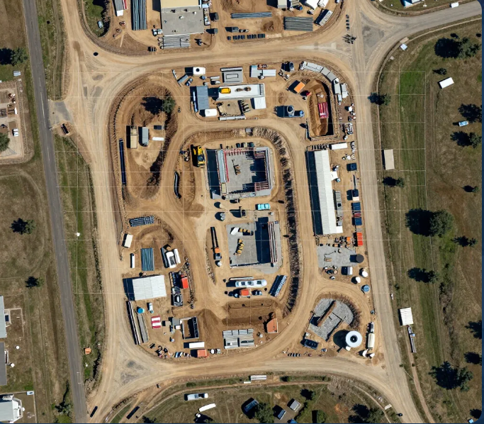Aerial view of a large construction site with roads, dirt lots, buildings, and parked equipment.