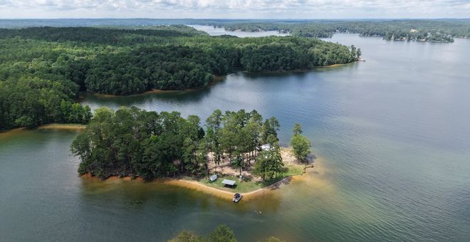 Small wooded island with a sandy shore in a calm lake, surrounded by dense forest and water