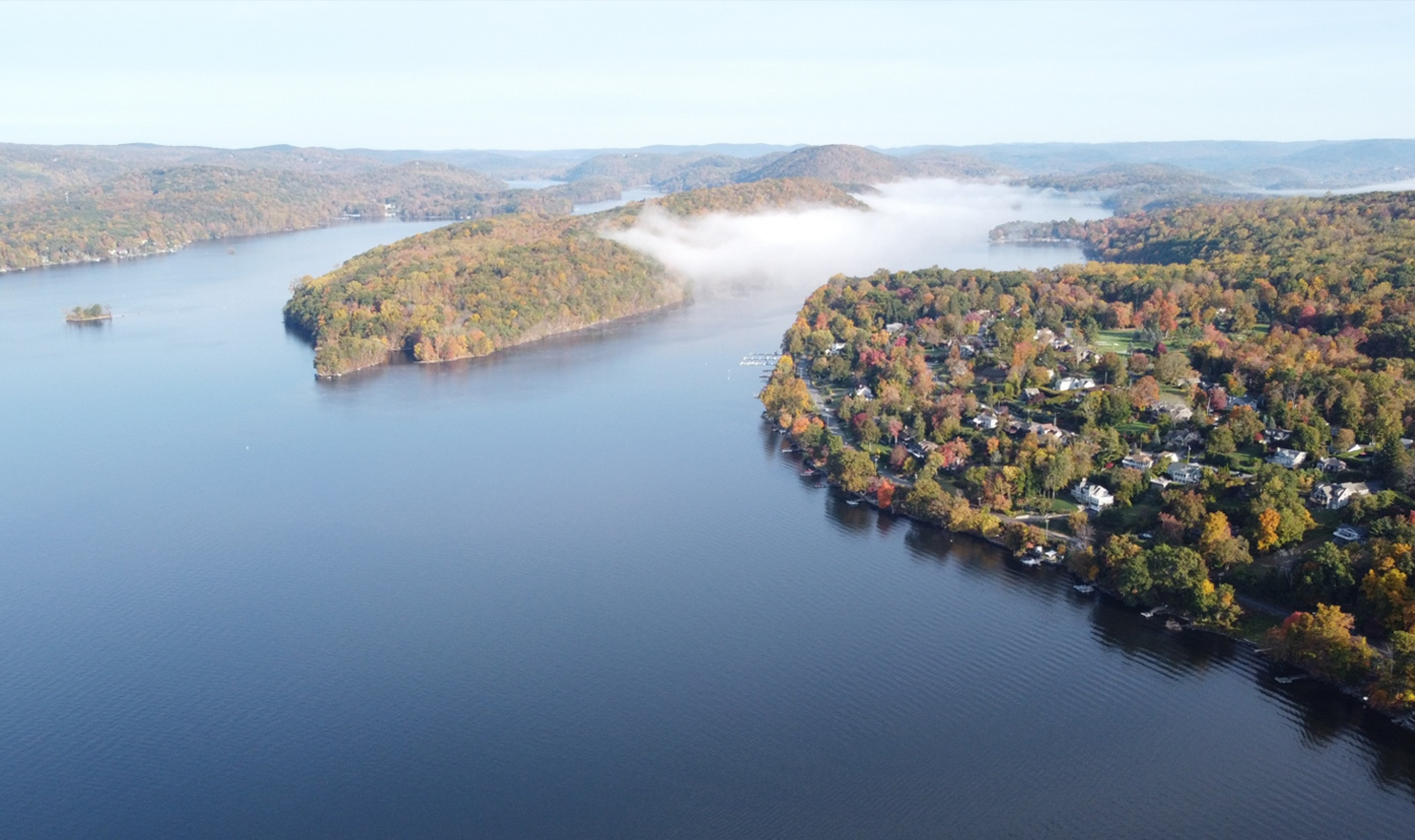 An aerial view of a lake surrounded by trees on a foggy day.