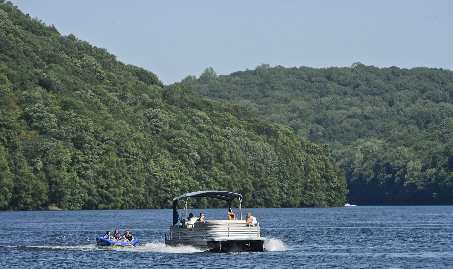 A boat with people on it is floating on a lake surrounded by trees.